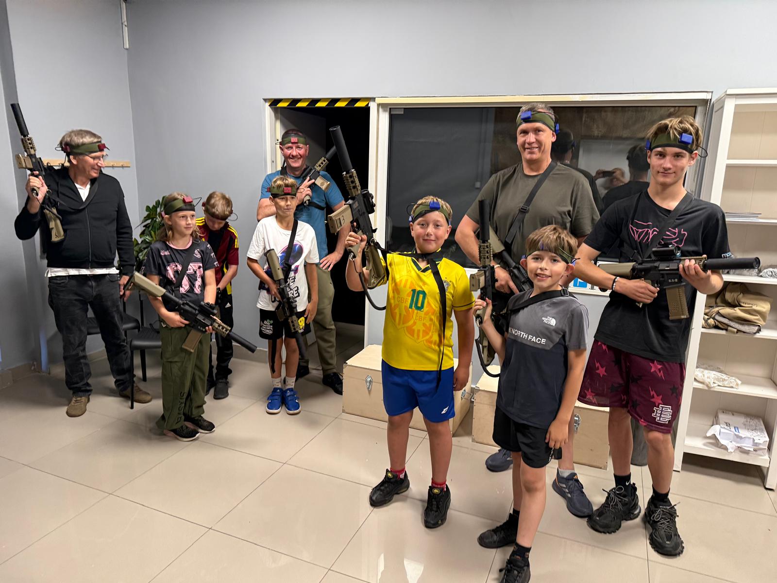 Duża grupa dorosłych i dzieci z pełnym wyposażeniem laser tag przed sesją gry